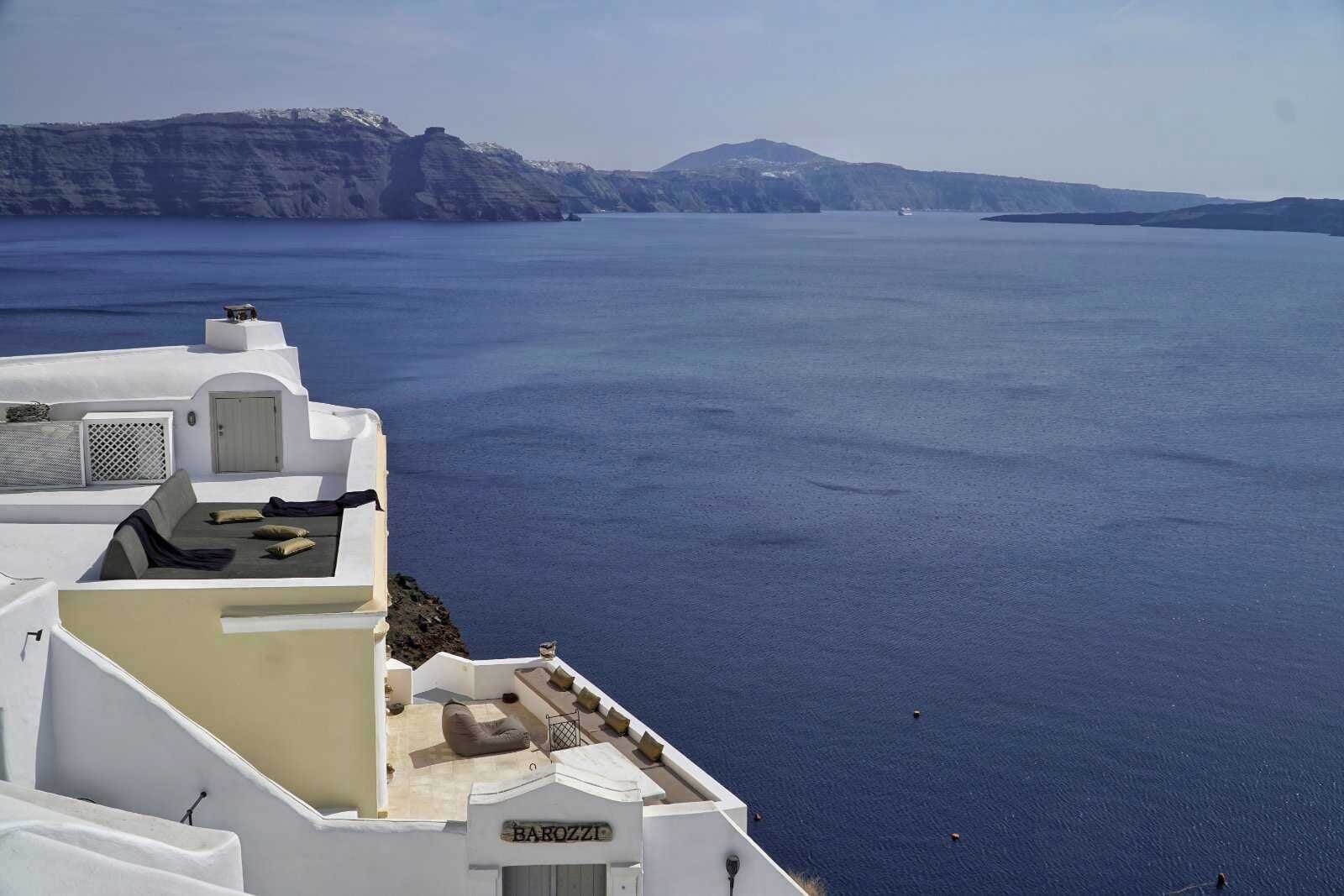 A seaside hotel with a terrace overlooking the ocean, featuring a white building with a sign reading "BAROZZI".