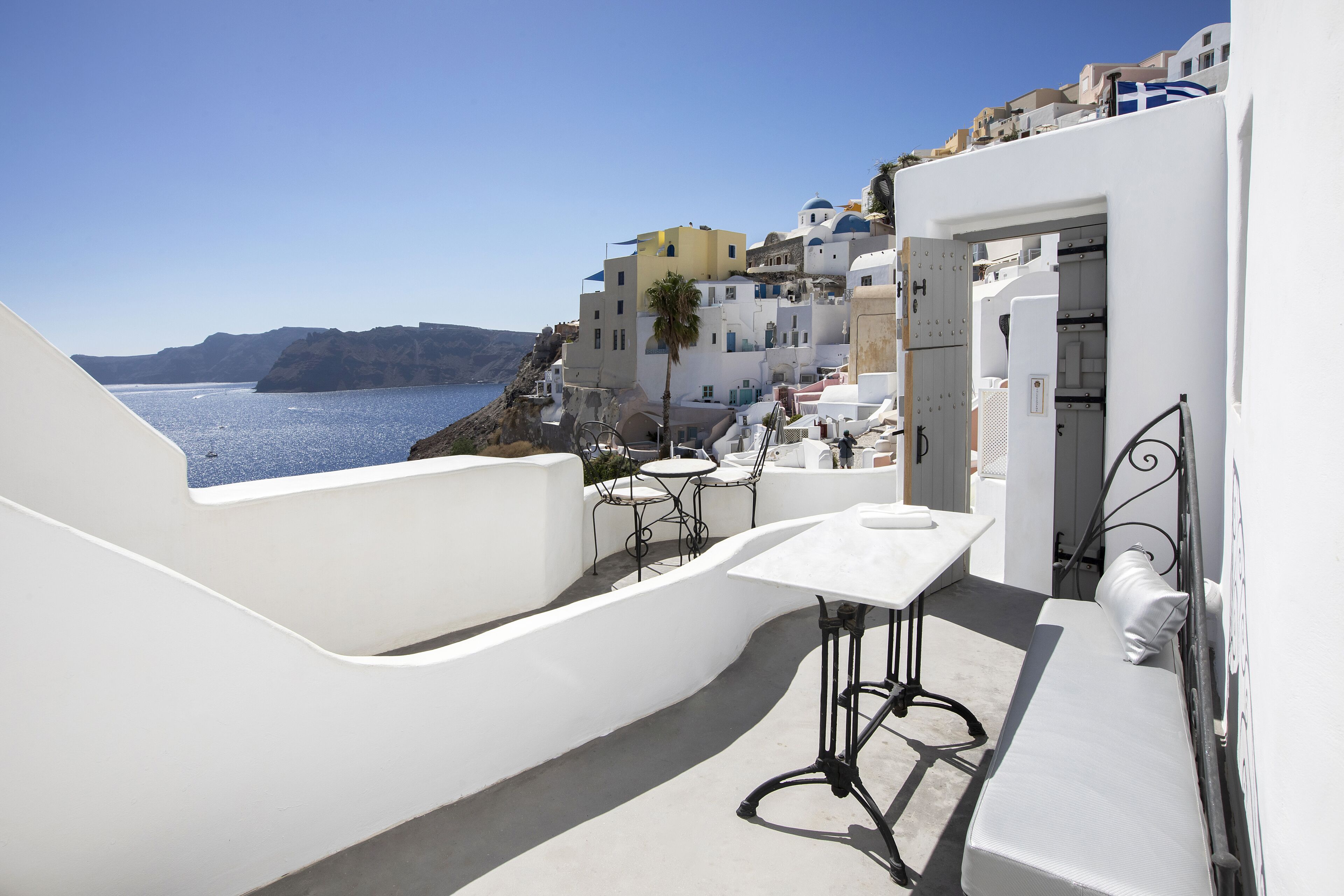 A white building with a balcony overlooking a body of water and a mountainous landscape.
