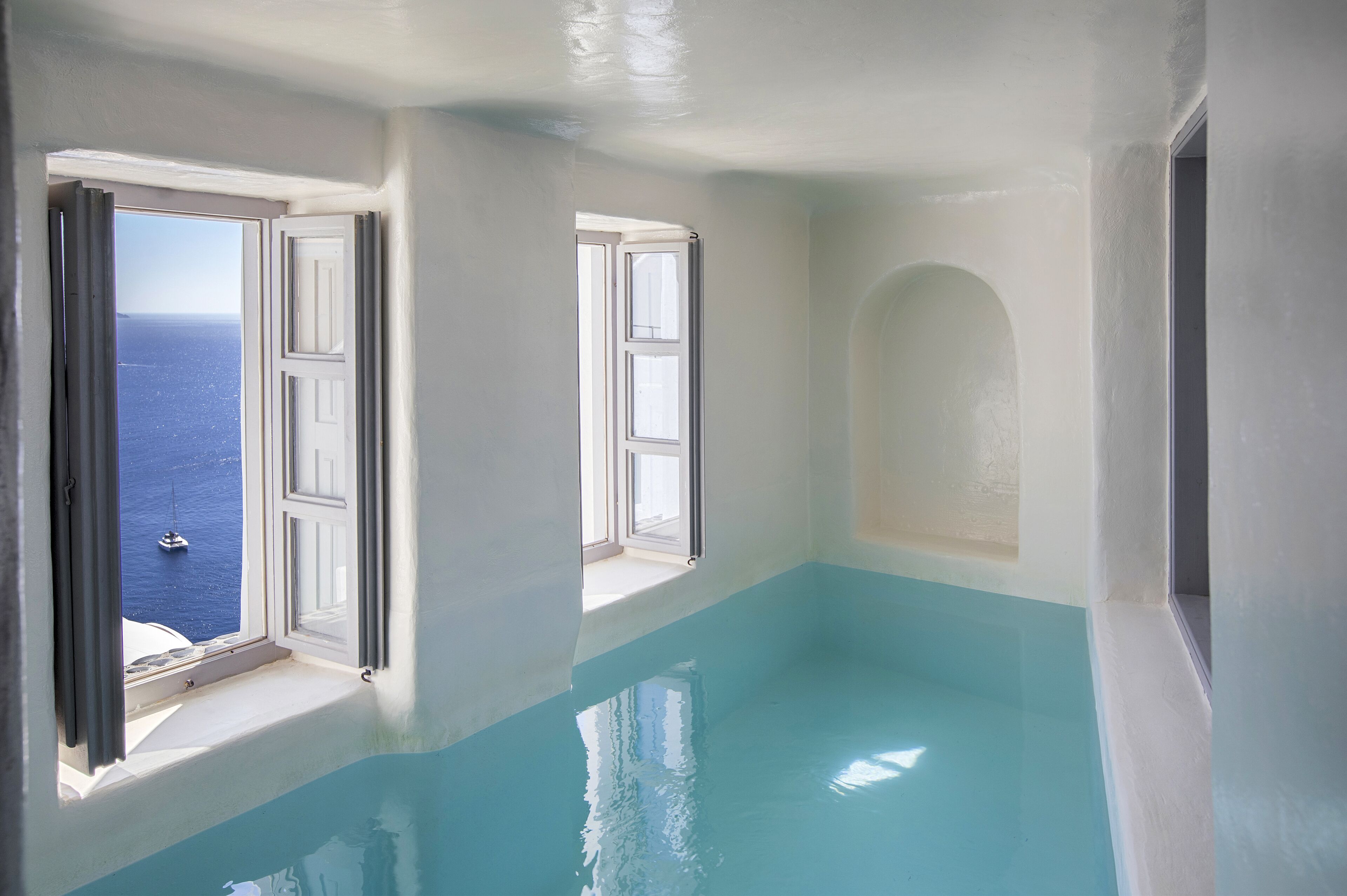 A room with a view of the sea through two open windows, a built-in bathtub, and a small alcove.