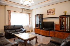 A living room with a black leather sofa, a wooden coffee table, a TV, and a cabinet with glass doors.