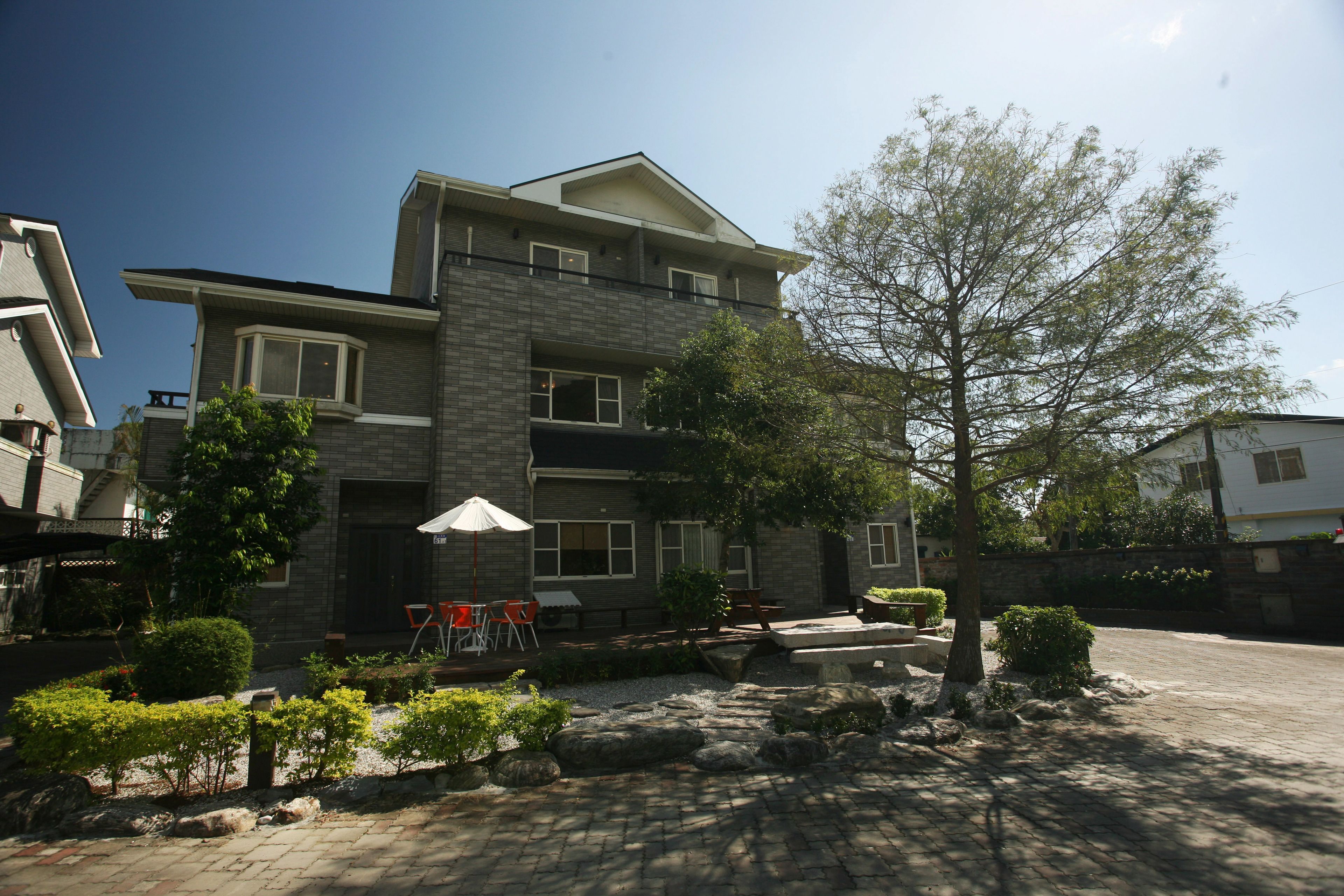 A modern two-story house with a stone facade, a covered patio with outdoor furniture, and a well-maintained garden.