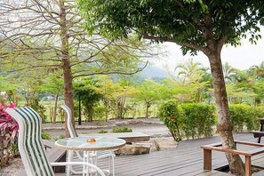 Una terrazza esterna con tavolo e sedie in vetro, immersa nel verde e alberi.