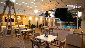 An outdoor patio area with tables and chairs, a hanging chair, and a pool. - Othello Hotel (Mersin)
