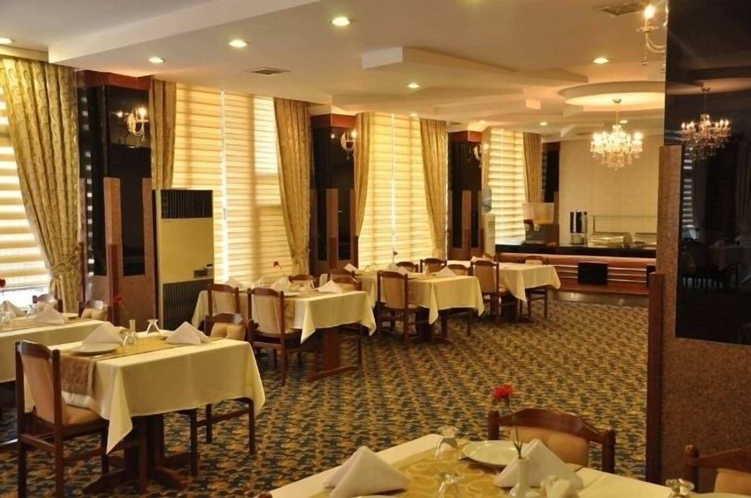 A dining area with tables set for service, a chandelier, and curtains.