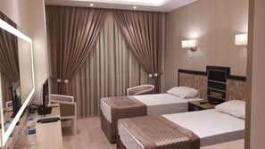 A hotel room with two beds, a desk with a computer and a phone, a mirror, and a window with curtains. - Othello Hotel (Mersin)