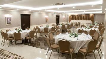 A banquet hall with round tables, beige chairs, and white tablecloths.