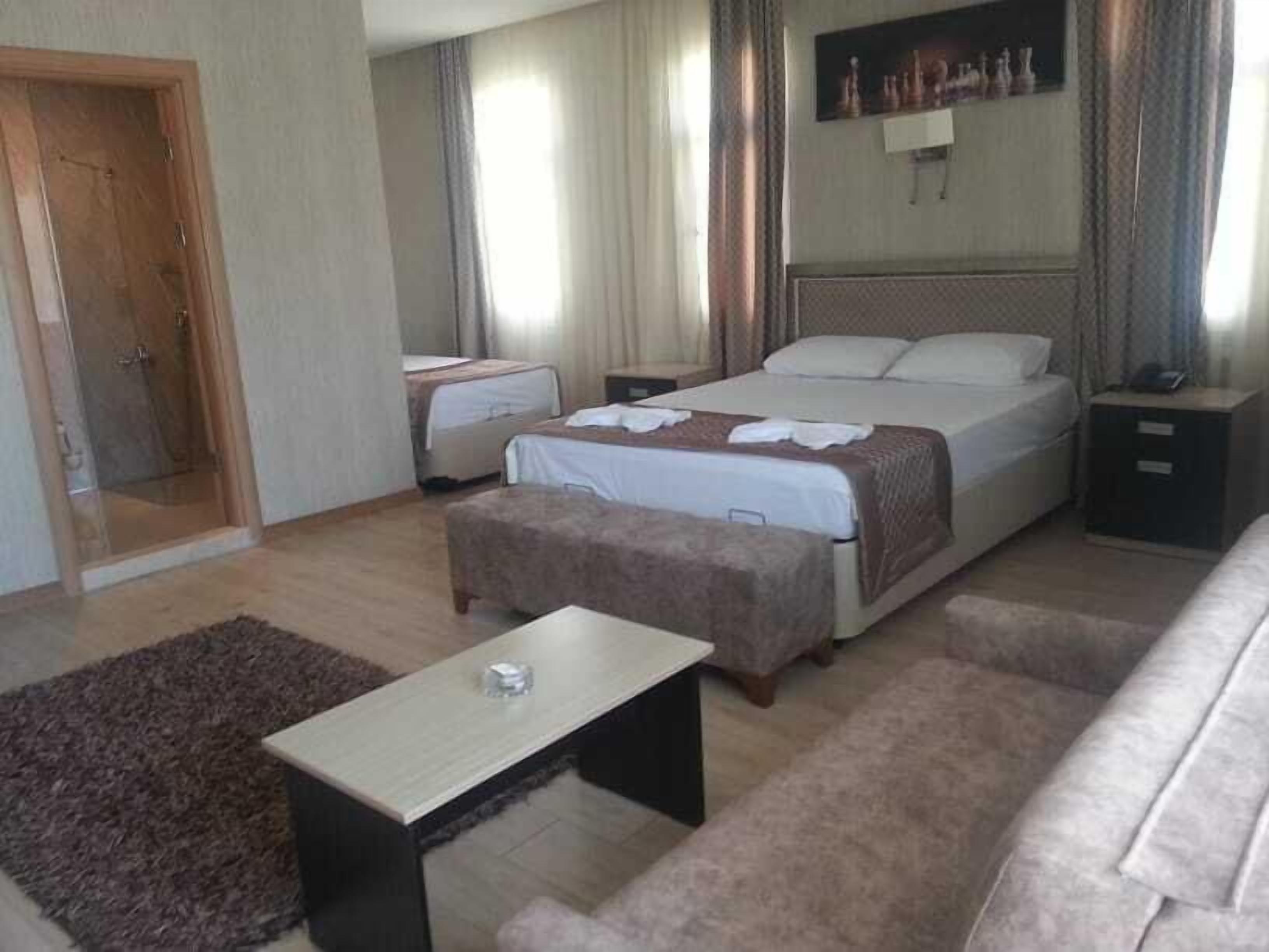 A hotel room with a bed, a bedside table, a small desk, a chair, a sofa, and a door.