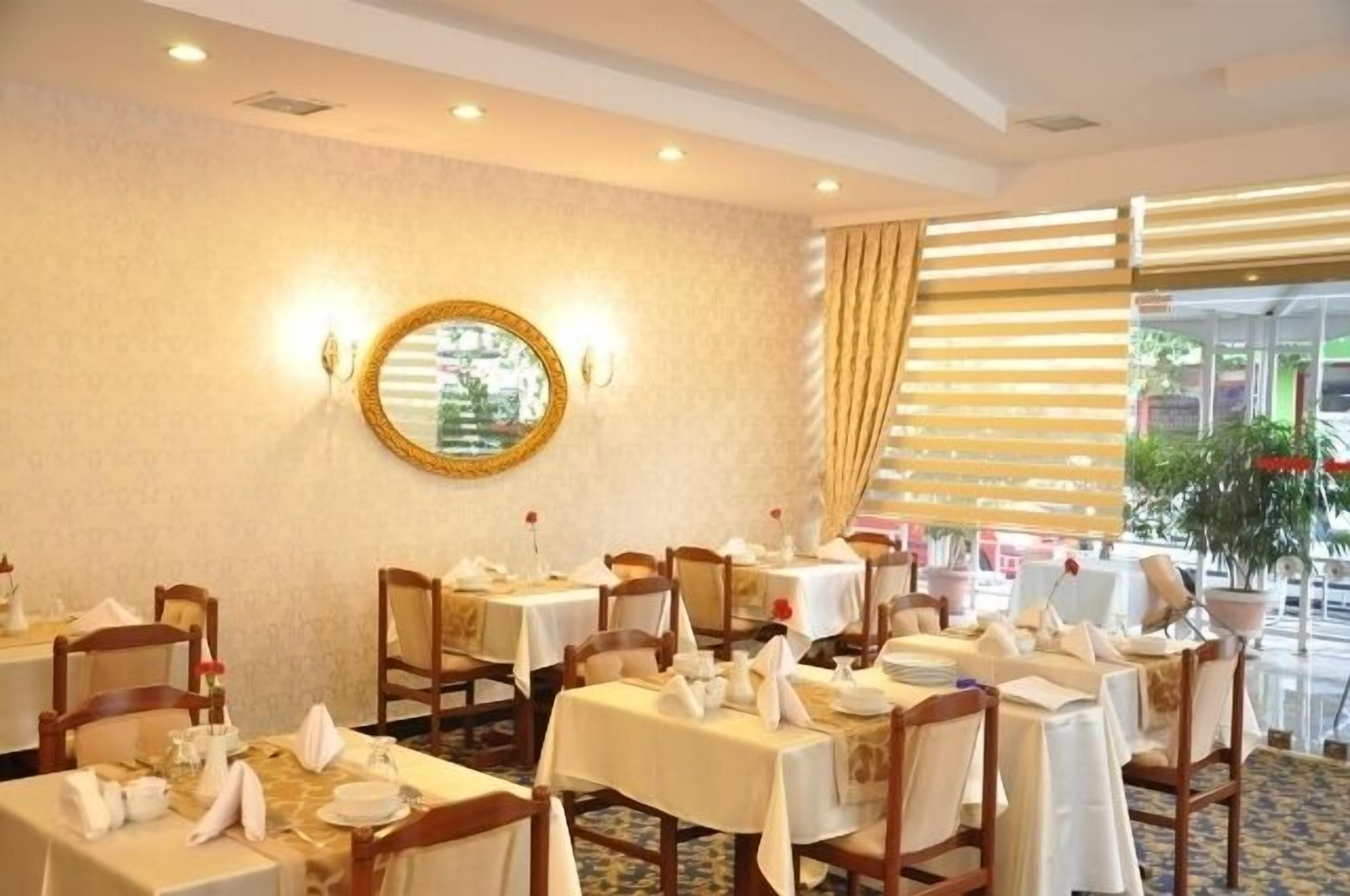 A dining area with tables set for service, a mirror on the wall, and a view of the outdoors through large windows.