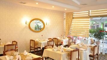 A dining area with tables set for service, a mirror on the wall, and a view of the outdoors through large windows.