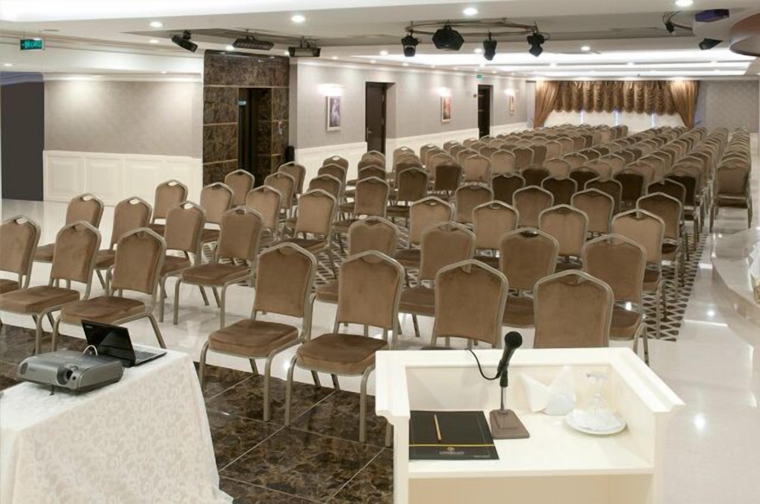 Un salón de conferencias con hileras de sillas, un atril con un ordenador portátil y un proyector.