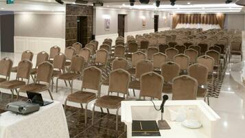 Un salón de conferencias con hileras de sillas, un atril con un ordenador portátil y un proyector.