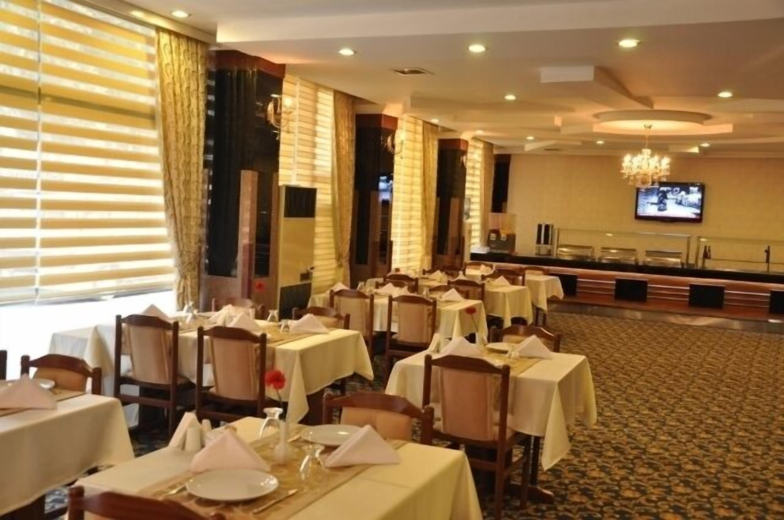 A hotel dining area with multiple tables and chairs, a chandelier, and a television screen on the wall.