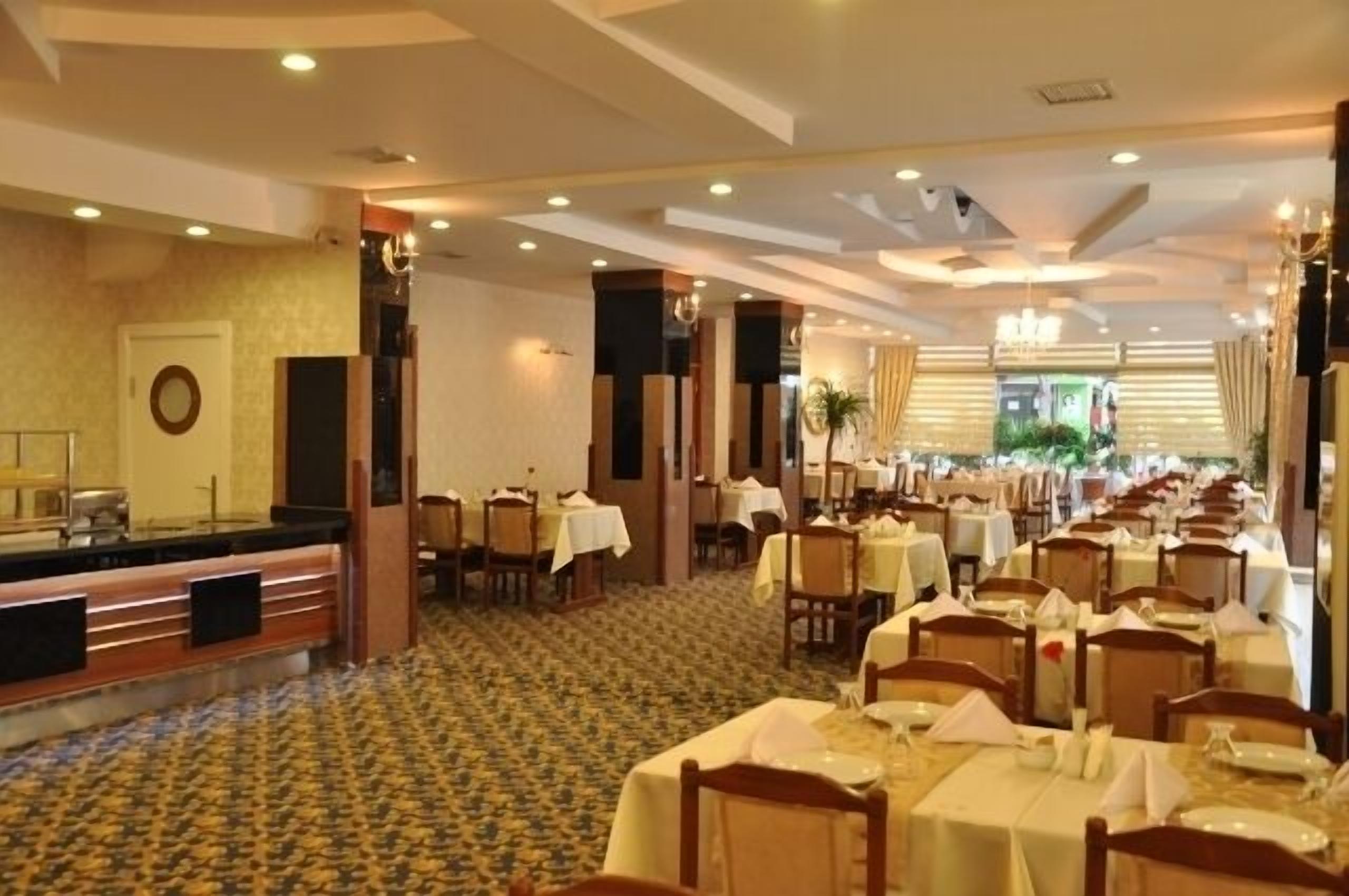 A spacious hotel dining area with multiple tables and chairs, a reception desk, and a patterned carpet.