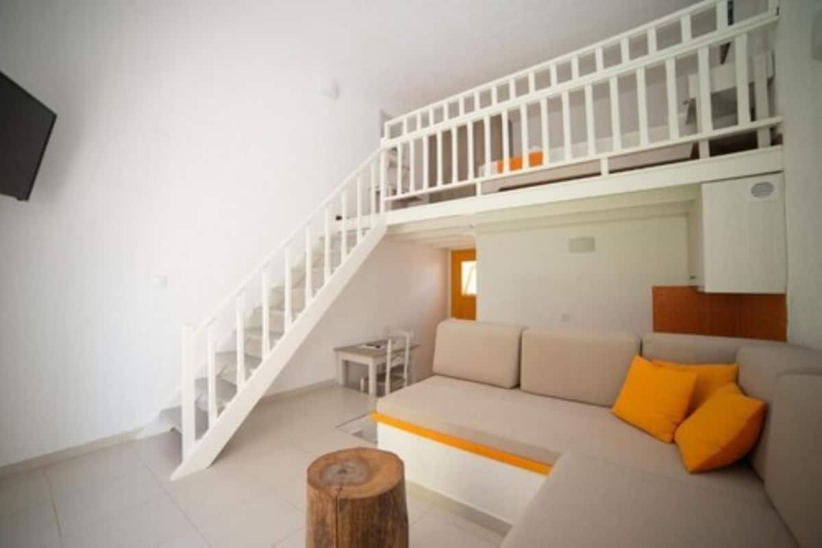 A living room with a sofa, a wooden stool, and a staircase leading to an upper level.
