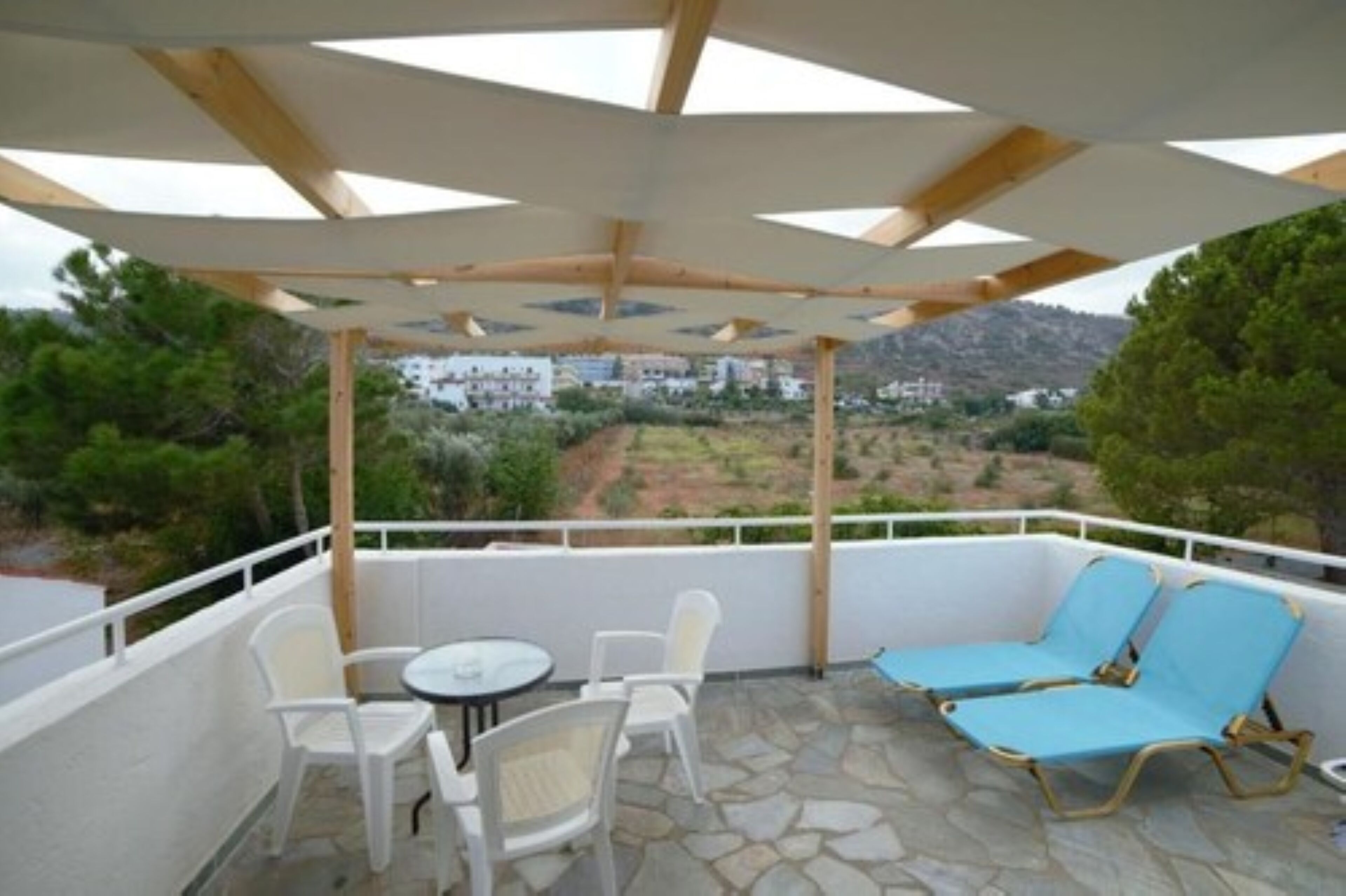 A covered outdoor seating area with white chairs and a table, overlooking a scenic landscape.