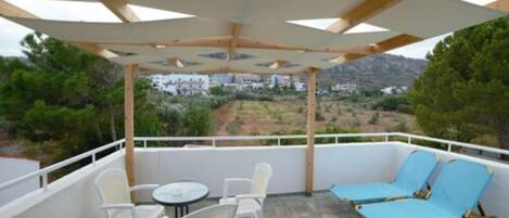 A covered outdoor seating area with white chairs and a table, overlooking a scenic landscape.