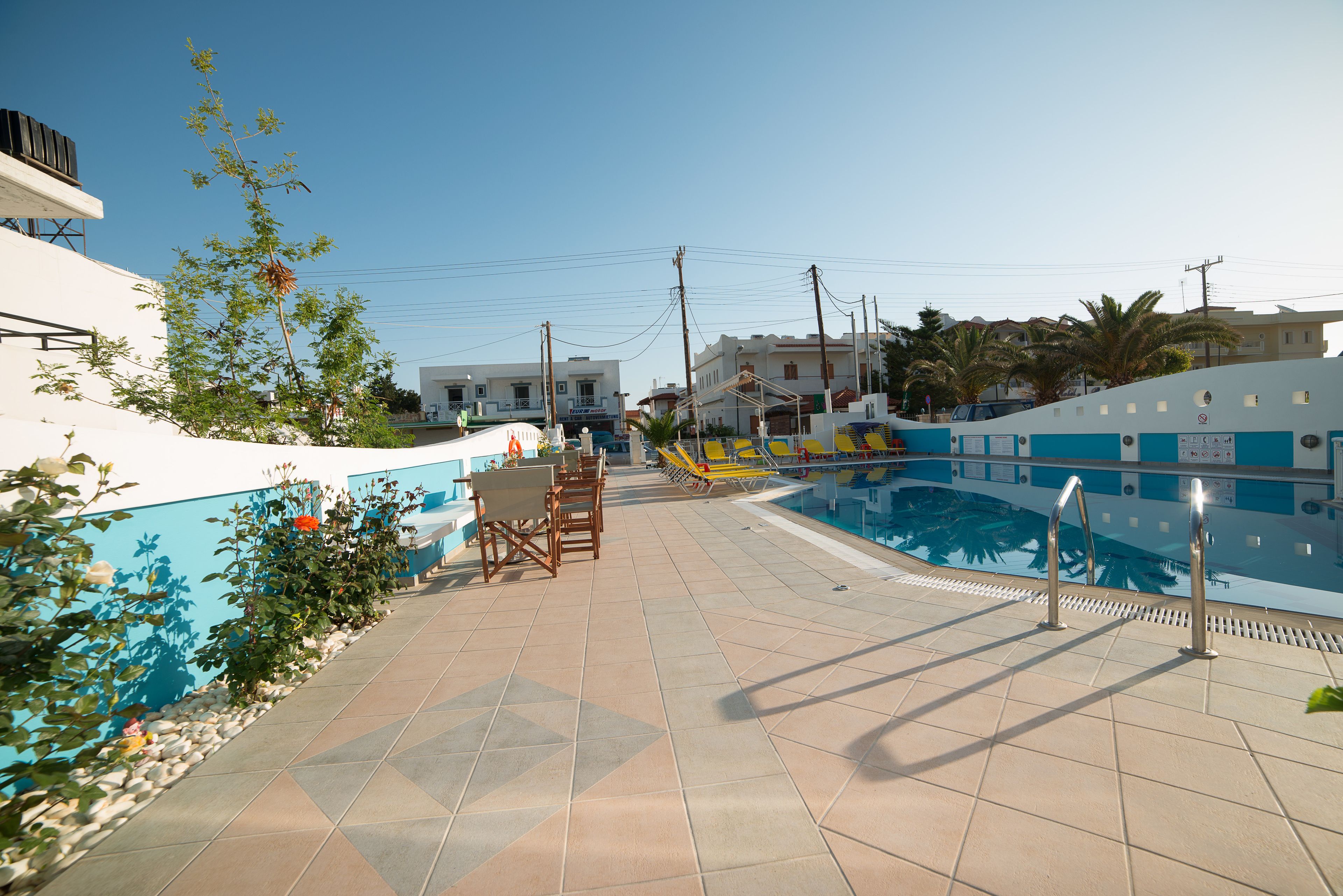 Un área de piscina con suelo de baldosas, sillas de descanso y un cielo azul despejado.