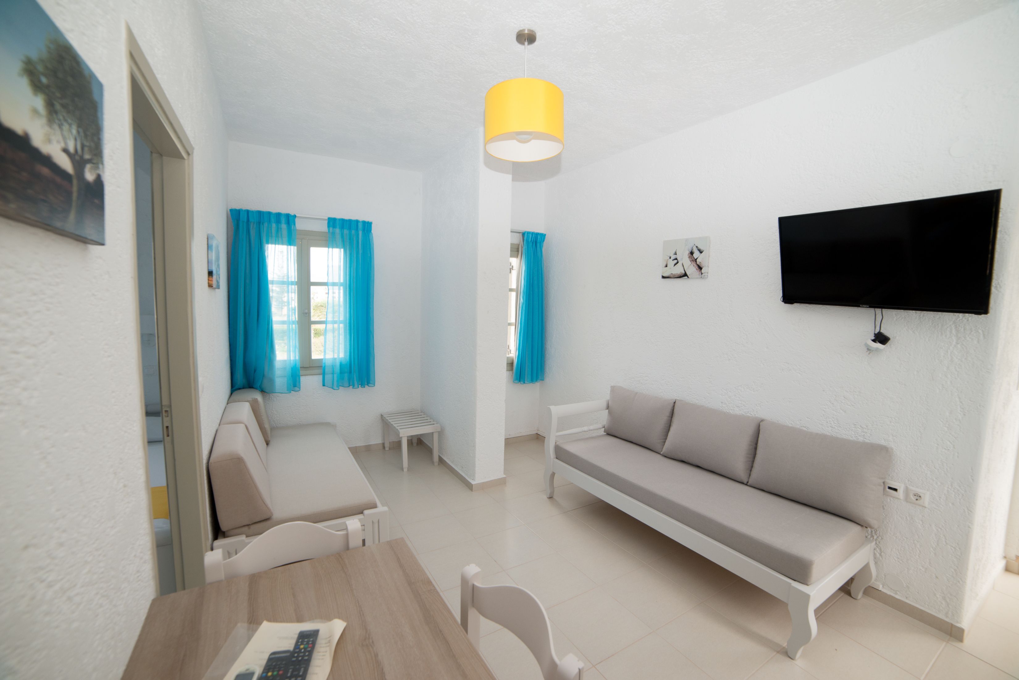A modern living room with a sofa, a dining table, and a TV mounted on the wall.