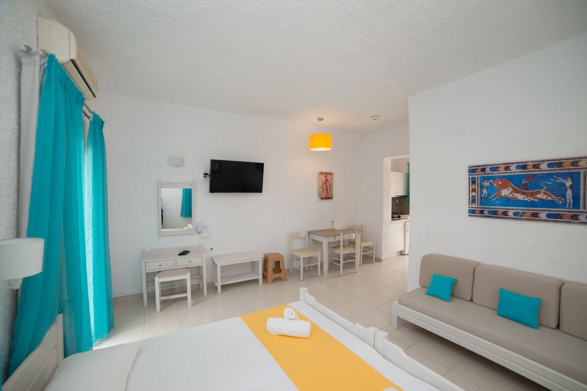 A hotel room with a bed, a desk, a chair, a sofa, a TV, and a painting on the wall.