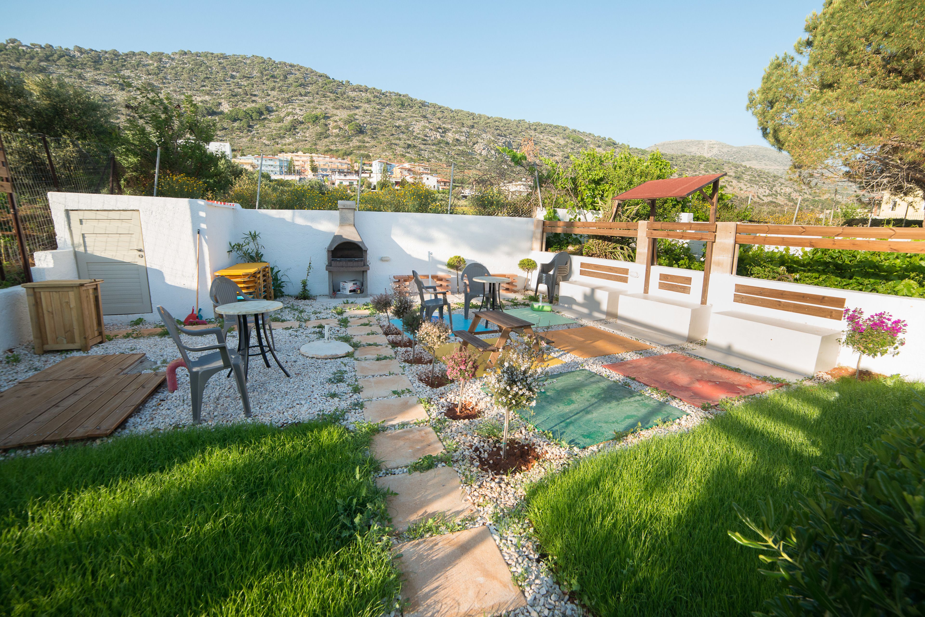 A patio with outdoor furniture, a barbecue grill, and a small pool area surrounded by greenery and a white wall.