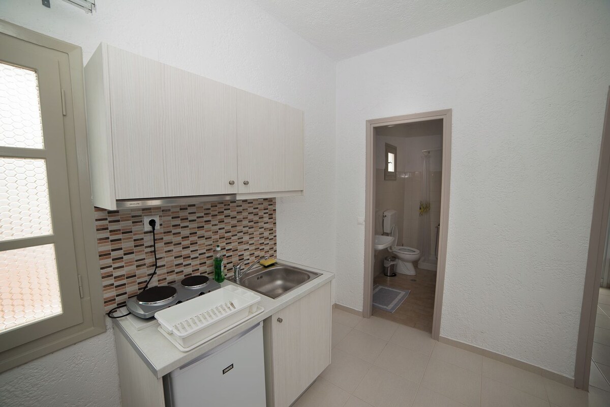Una cocina compacta con armarios blancos, salpicadero azulejado, un lavabo y un refrigerador pequeño.