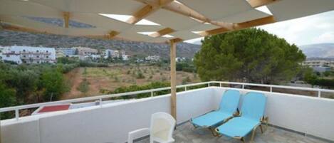 A balcony with a table and chairs, a wooden pergola, and a view of a hillside with buildings.