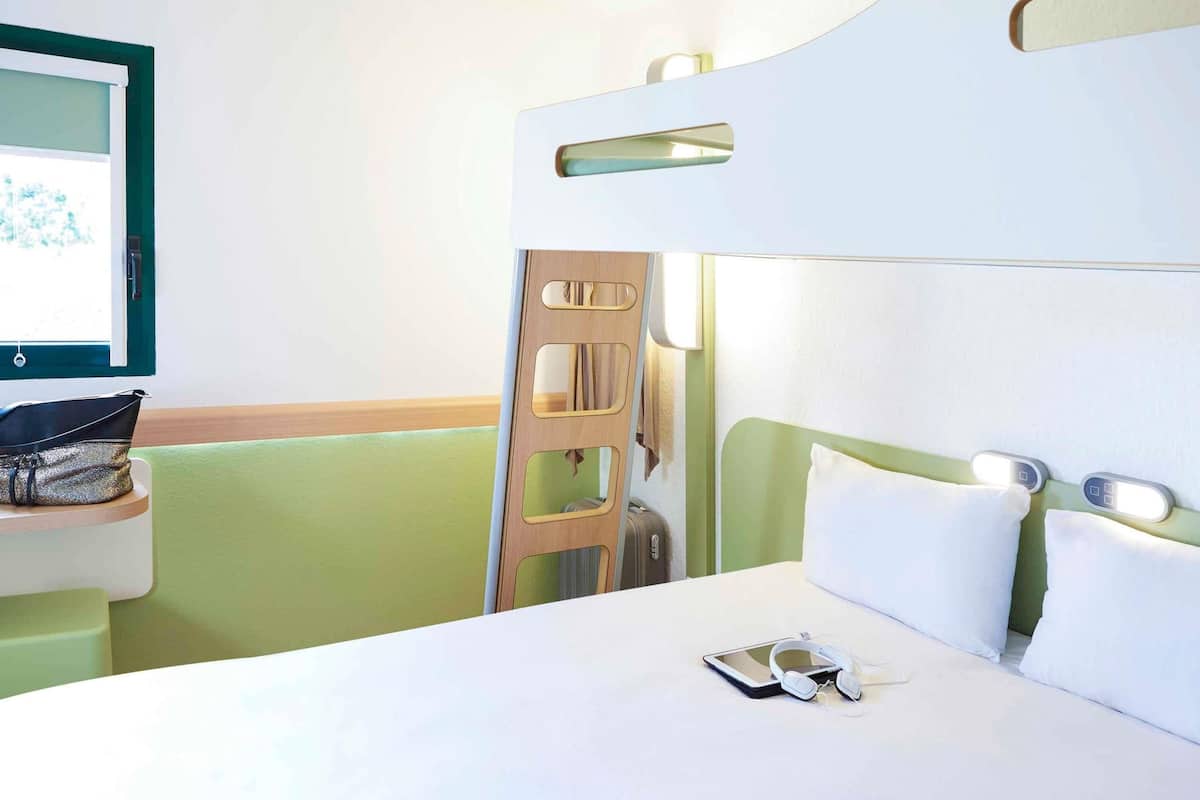 Un lit superposé avec une table de chevet, un téléviseur fixé au mur et une valise posée sur le sol.