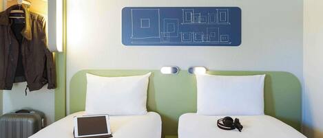 Habitación de hotel con dos camas, una mesita de noche con una tableta, una maleta y un perchero con chaquetas.
