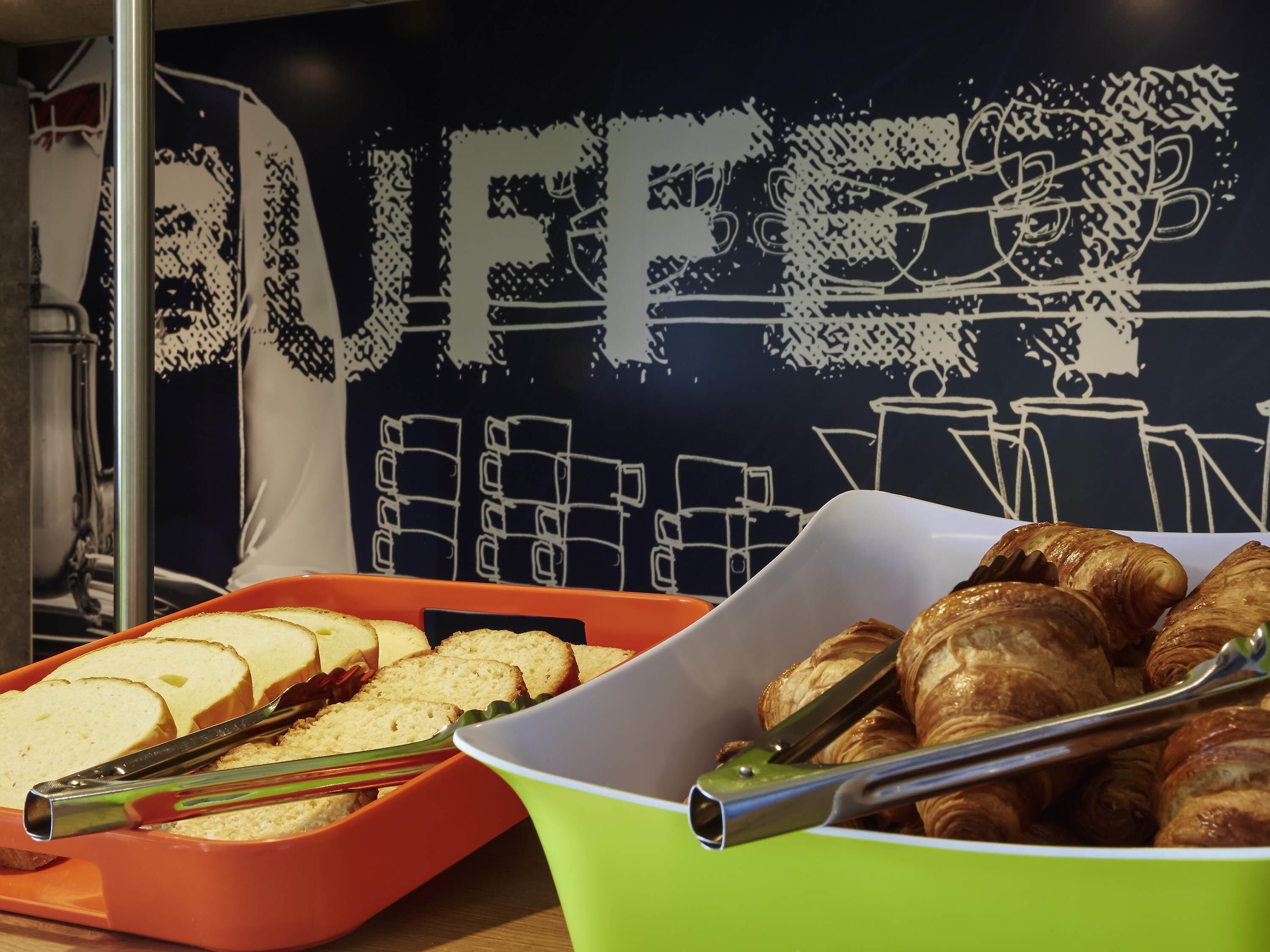 A buffet with bread and croissants, tongs, and a wall with a 'BUFFET' sign.