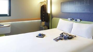 A hotel room with a bed, a bedside table, a lamp, a wall with a geometric design, and a window.