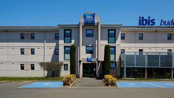 A building with 'ibis budget hotels' signage, a parking lot with blue handicapped parking spaces, and a clear sky.