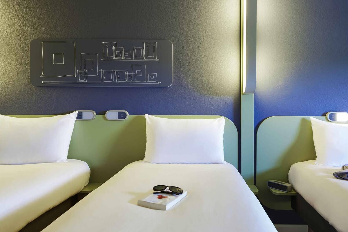 Une chambre d’hôtel avec deux lits, un panneau de commande fixé au mur et une table de chevet avec une télécommande.