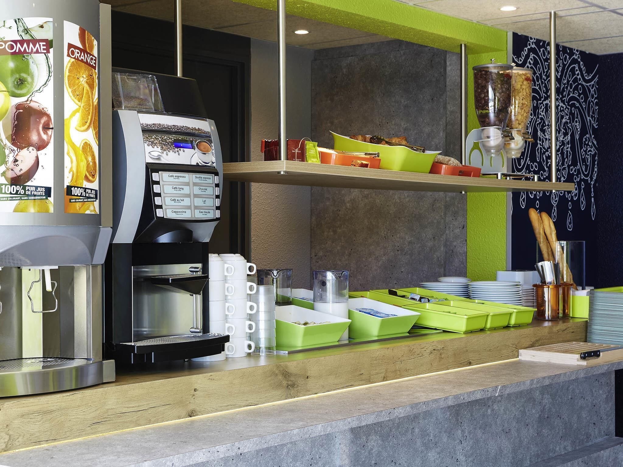 Una máquina de café con un panel de selección, un dispensador de café y una encimera con contenedores y utensilios verdes.