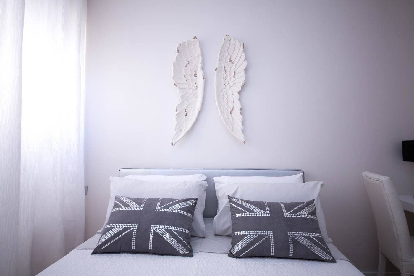 Un dormitorio con una cama, dos almohadas con estampado de la bandera británica y dos adornos de pared con forma de alas.