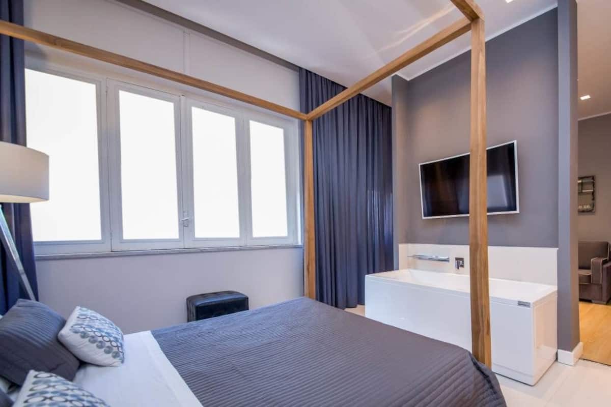 Une chambre d’hôtel moderne dotée d’un grand lit, d’un téléviseur intégré, d’une salle de bain séparée avec baignoire et d’un petit coin salon.
