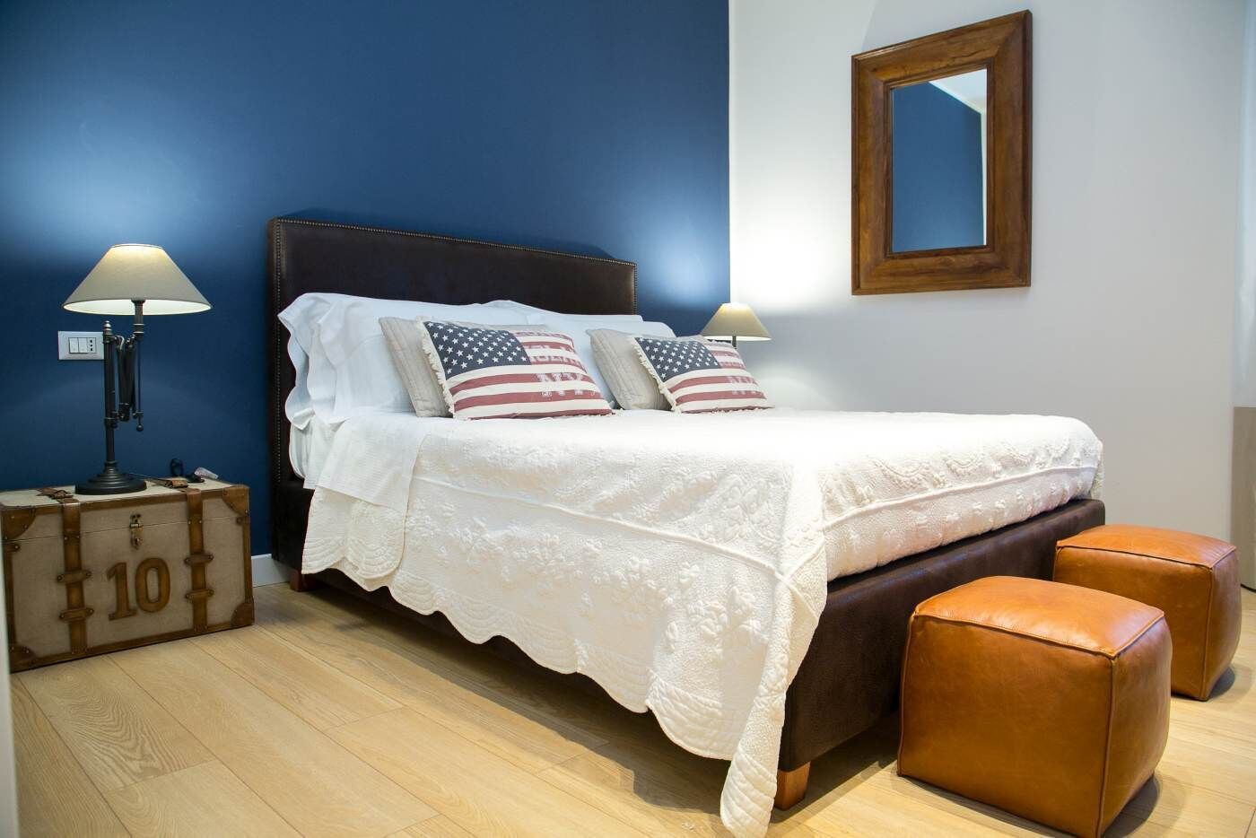 Un dormitorio con cama, almohadas, lámpara, maleta y espejo.