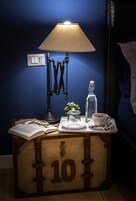 Un comodino con una lampada, una bottiglia, una tazza, bicchieri e un libro aperto.