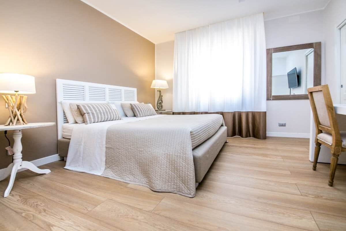 Une chambre à coucher avec un lit, des tables de chevet, une chaise, un miroir et une fenêtre avec des rideaux.