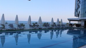 Un área junto a la piscina con sillones de descanso y sombrillas, vista despejada al mar y una estructura de edificio moderna.