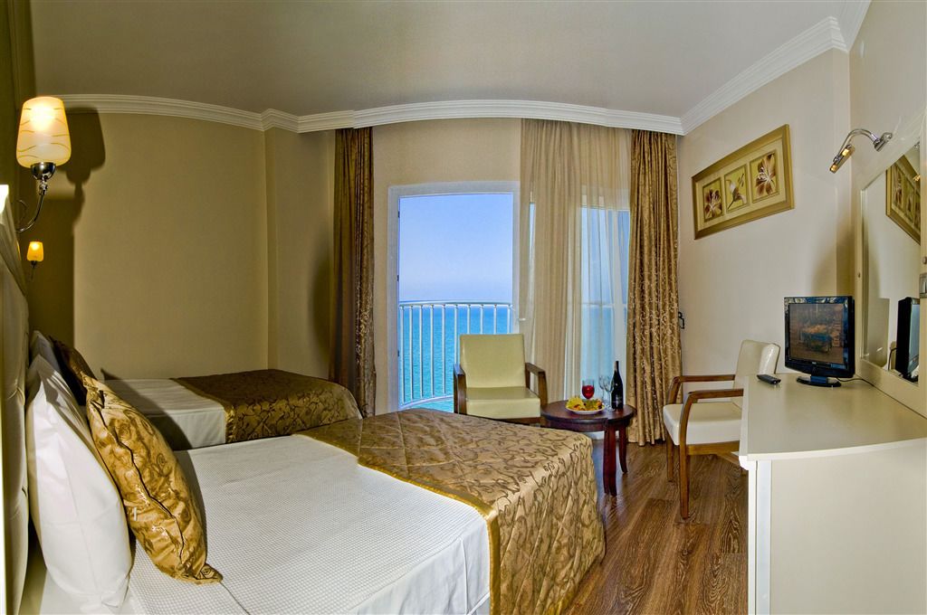 A hotel room with two beds, a desk with a computer, a chair, and a view of the sea.
