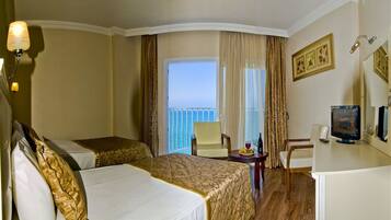 A hotel room with two beds, a desk with a computer, a chair, and a view of the sea.