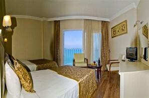 Habitación de hotel con dos camas, un escritorio con computadora, una silla y vista al mar.