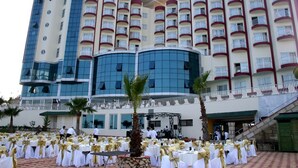 Un hotel con varios pisos, fachada de vidrio curvada y mesas al aire libre con manteles blancos y dorados.
