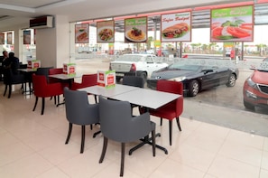 A restaurant with tables and chairs, a menu board, and a view of parked cars outside.