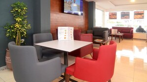 Een restaurant met een televisie aan de muur, een menukaart op de tafel en rode en grijze stoelen.