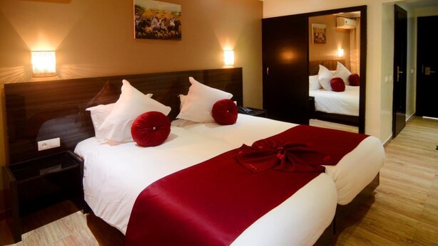 Een hotelkamer met een groot bed, twee nachtkastjes, een spiegel en een schilderij aan de muur.