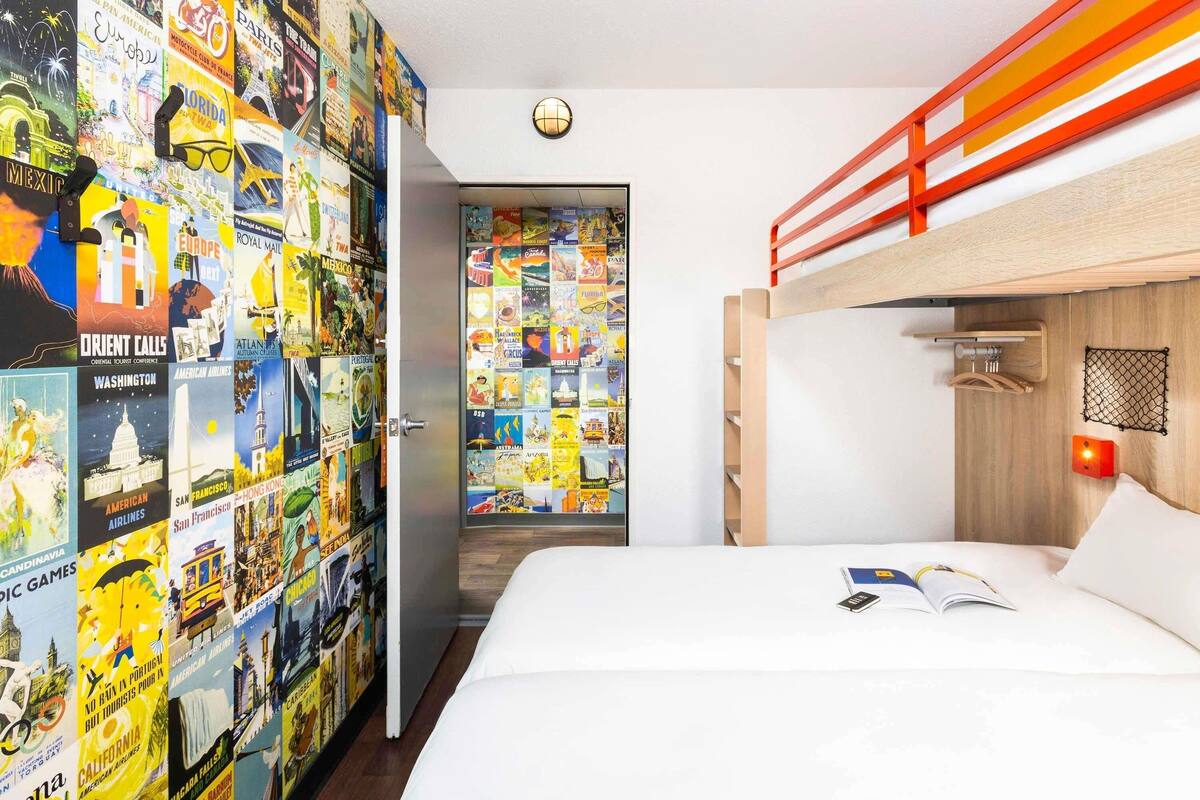 A bedroom with a bunk bed, a wall decorated with travel posters, a round light fixture, and a wooden headboard.