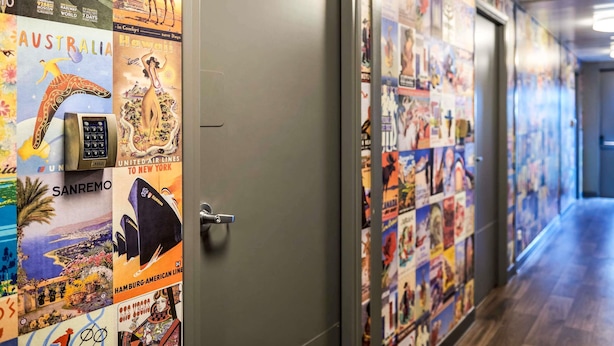 Un couloir orné d’affiches de voyage, une porte dotée d’une poignée et d’un système de verrouillage à clavier.