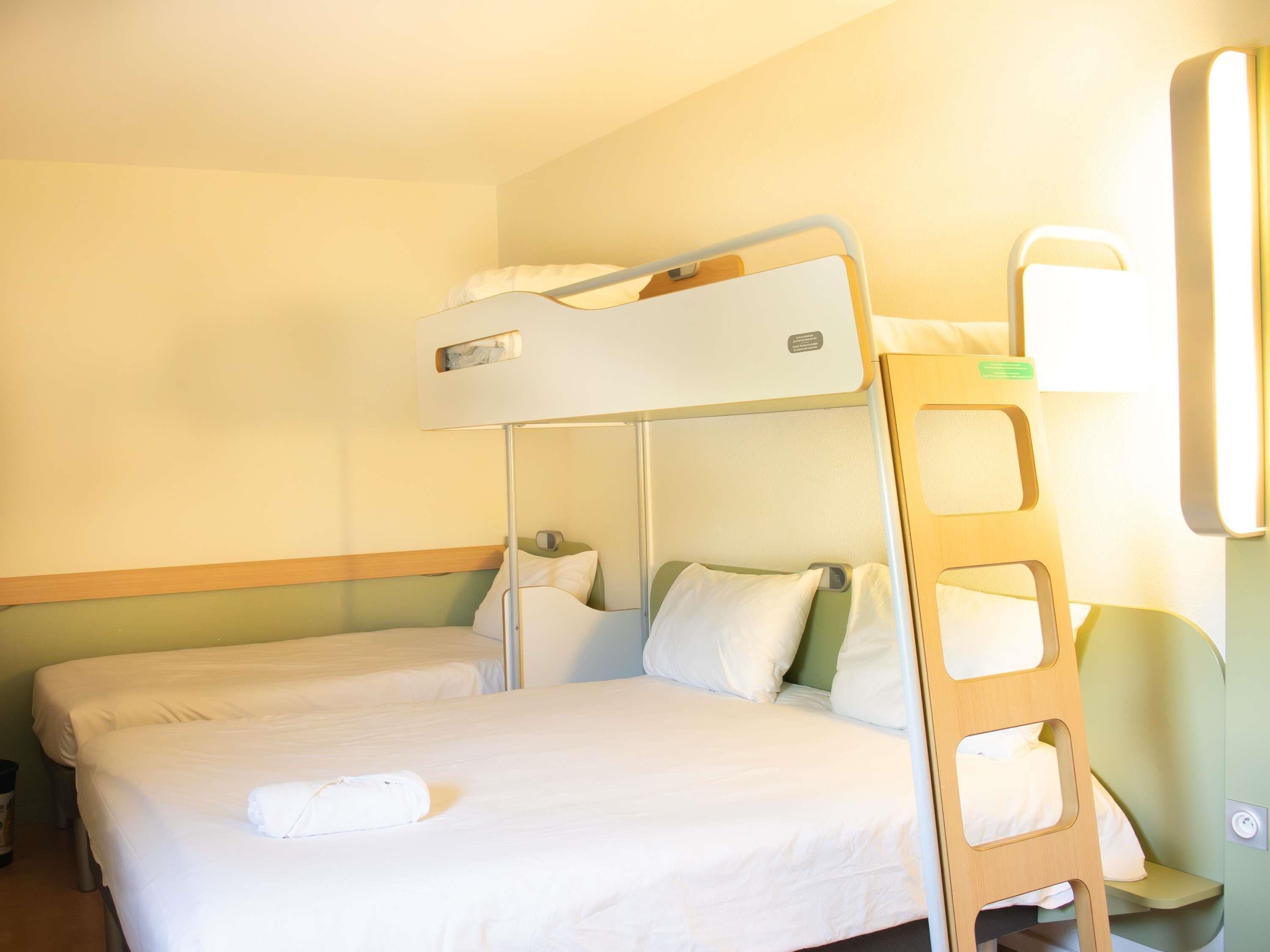 Dormitorio con literas, una mesita de noche y una lámpara fijada a la pared.