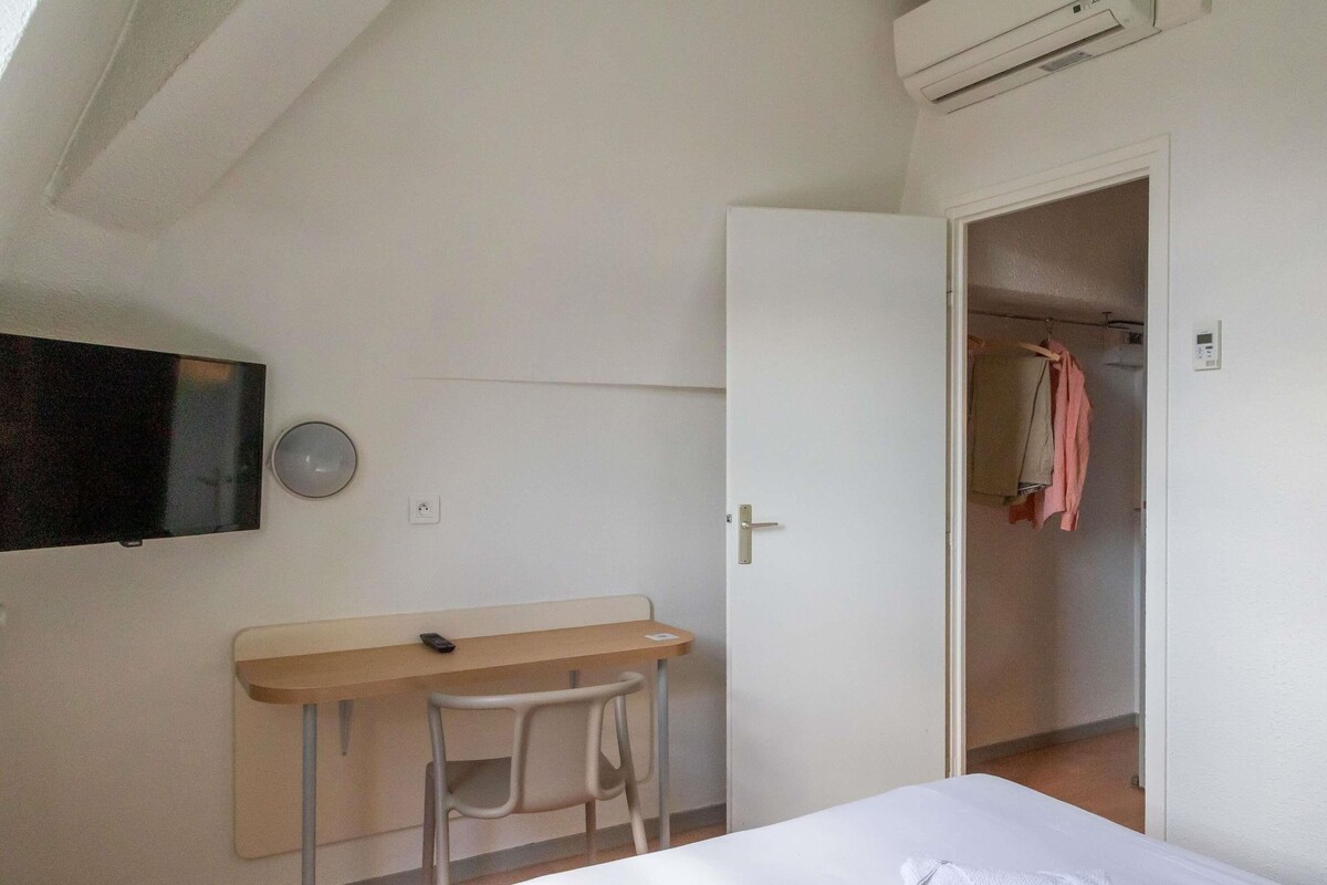 Un dormitorio con cama, escritorio, silla, televisión y armario abierto.